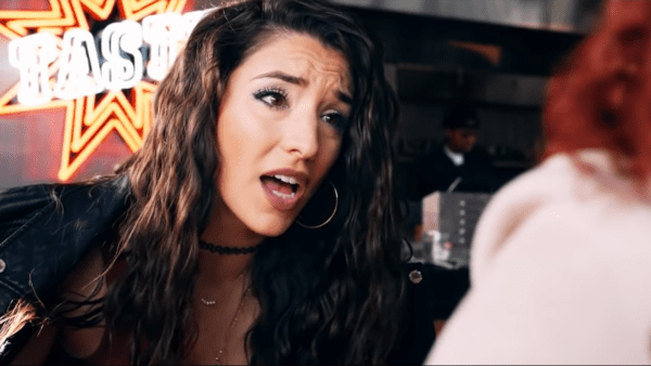 pretty woman with wavy brown hair talks animatedly in front of neon sign