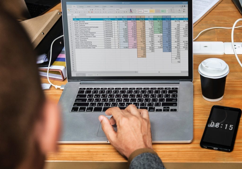 man at desk with laptop and spreadhsheet on screen