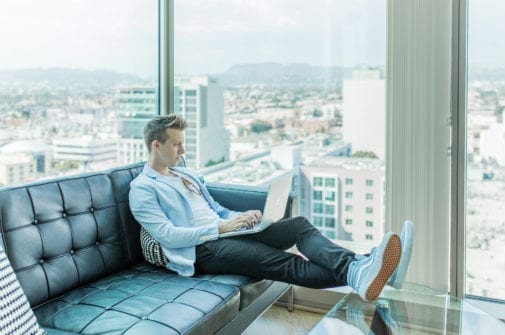 young man with blue vans sneakers sits on couch in los angeles apartment with a laptop entrepreneur