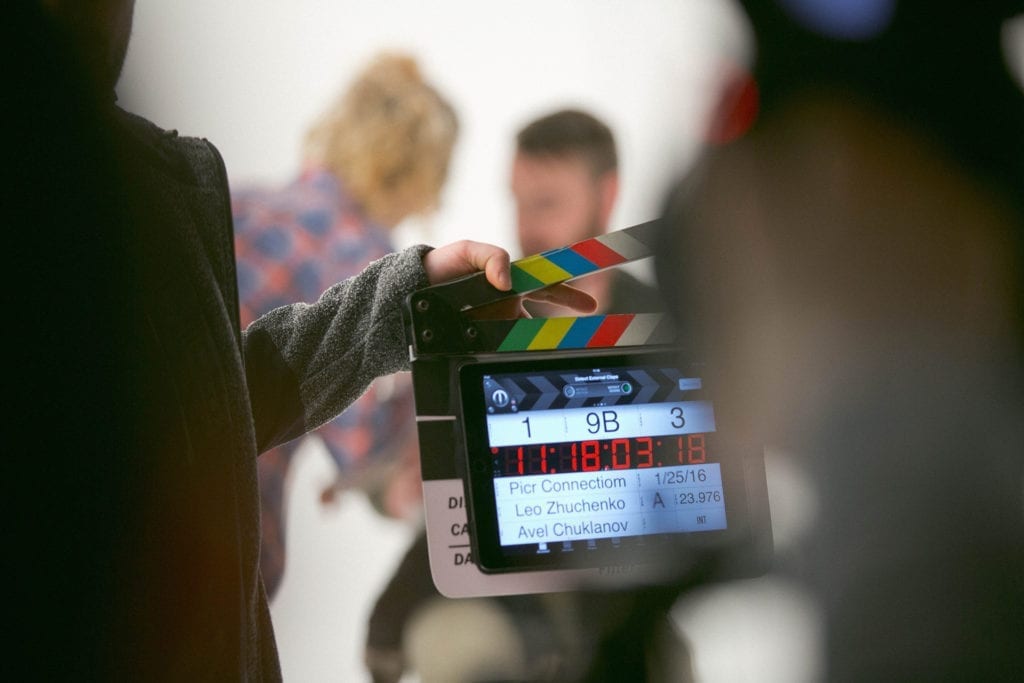 man holds digital film clapperboard slate on a film set with crew
