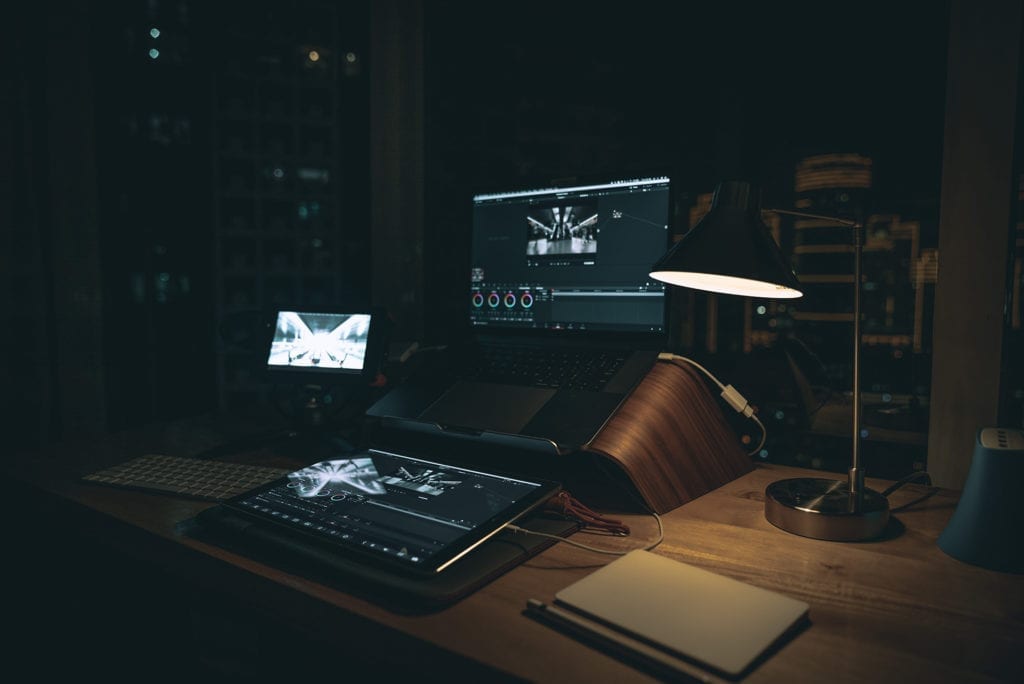 vide =o colorist editing equipment on wooden desk with multiple monitors and lamp