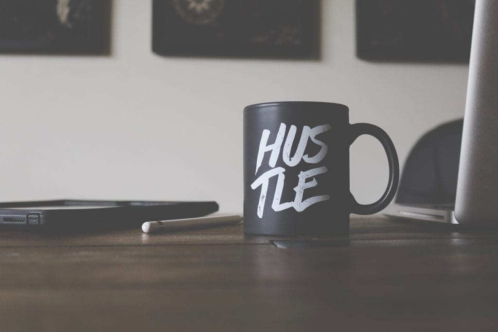 black mug with white script text that says hustle on a wooden table