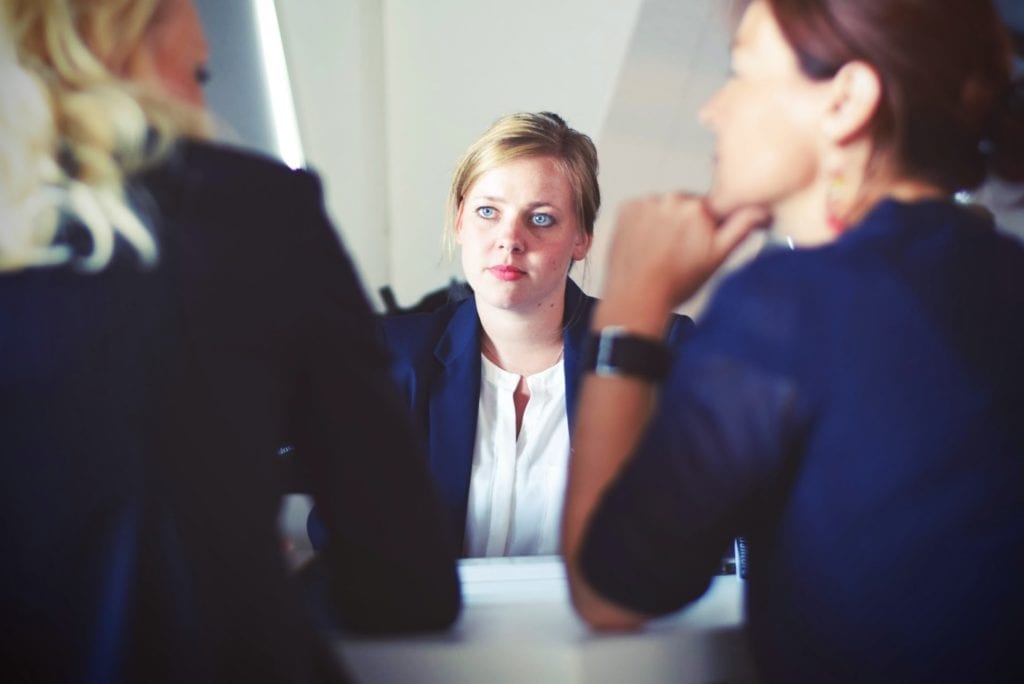 three women in business sitting beside table wearing suits