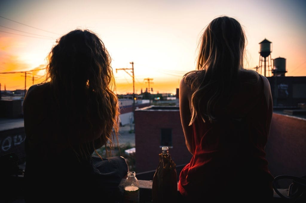 friends sit on rooftop with drinks watching sunset