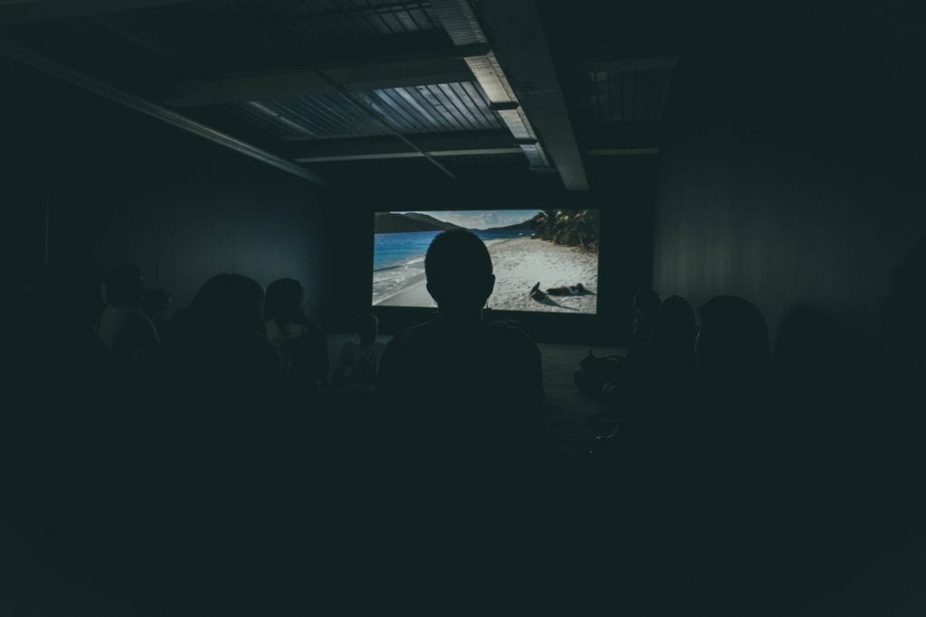 man standing in front of film projection in audience