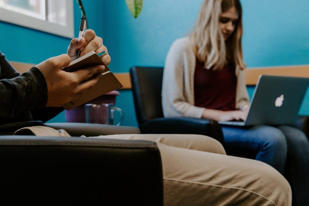 woman and man take notes on laptop and writing pad