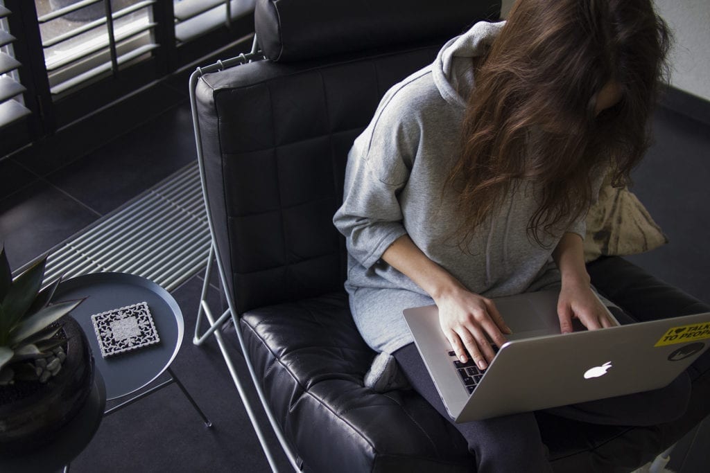 woman sits in chair editing at macbook laptop