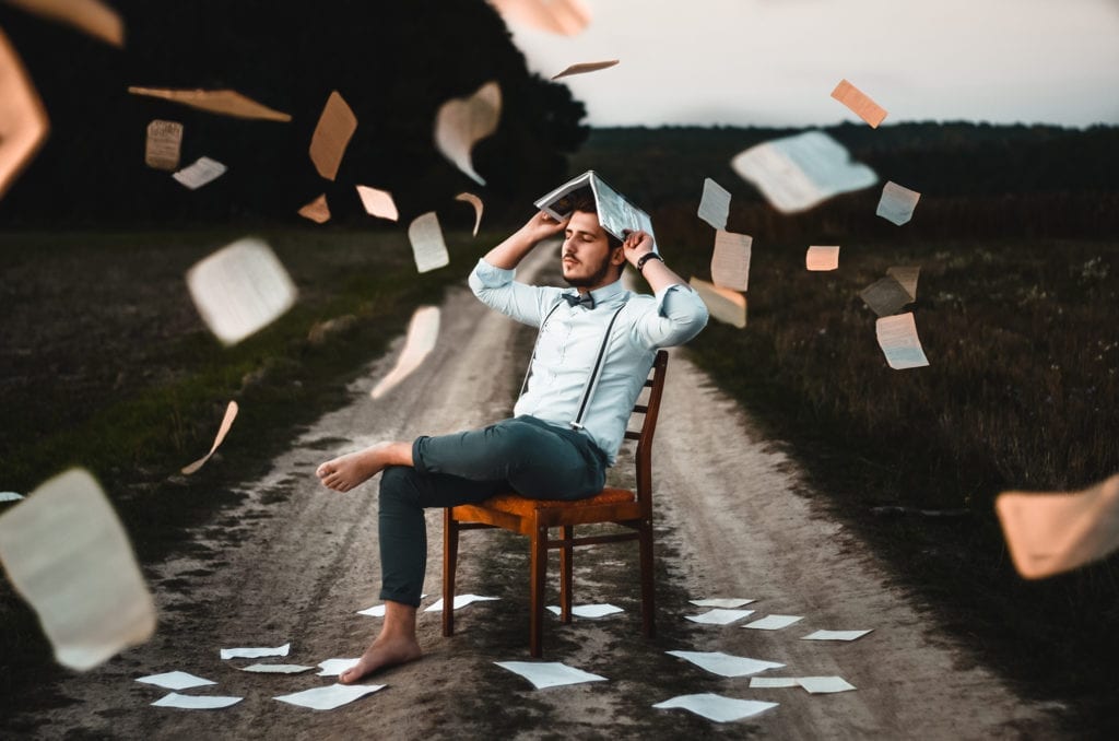 man sitting on dirt road with paper flying everywhere