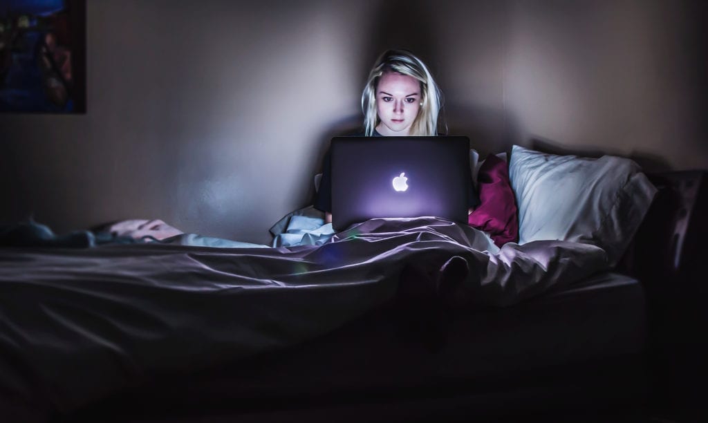 woman sitting on bed with macbook laptop and blanket