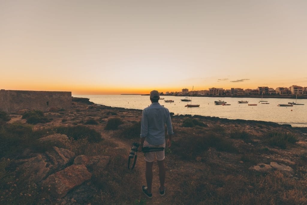 independent filmmaker standing by coast looking at sailboats