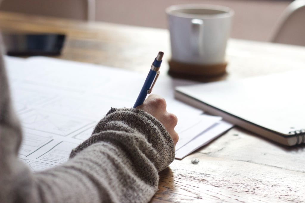 writer at desk with papers and pen and coffee mug