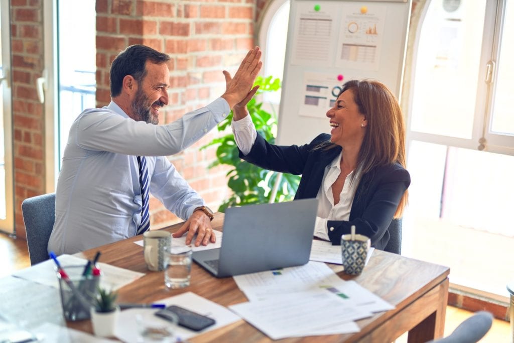 Two colleagues high five over a laptop film fund